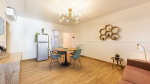 Eine moderne Küche mit Essbereich, einem Kühlschrank, einem runden Tisch mit Stühlen, einer sechseckigen Wanddekoration und einem kleinen Beistelltisch mit Pflanze.