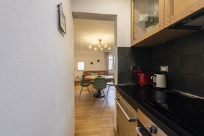 A modern kitchen with a black stove, a red coffee maker, and a dining area with a round table and green chairs.
