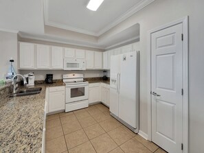 A kitchen with white cabinets, a granite countertop, a built-in oven, a microwave, and a refrigerator.