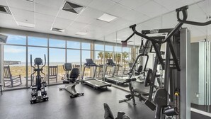 Un gimnasio con máquinas de cardio, equipo de pesas y amplios ventanales con vista al mar.