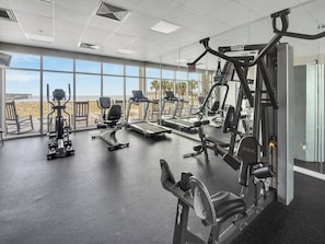 Una palestra con macchinari cardio, attrezzature per pesi e ampie finestre vista spiaggia.