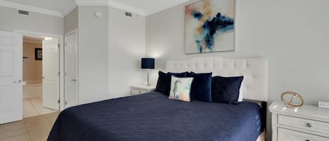 A bedroom with a large bed, white nightstands, a ceiling fan, and a painting on the wall.