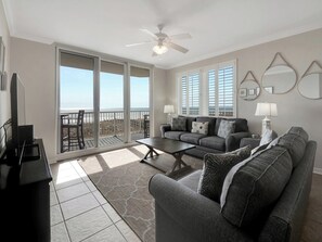 A spacious living room with a large sliding glass door leading to a balcony, a ceiling fan, and a sofa set.