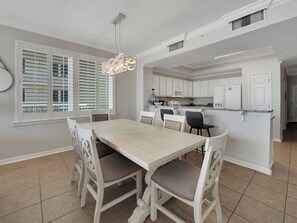 A dining area with a white table and chairs, a kitchen with white cabinets, and a pendant light.