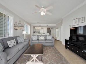 A spacious living room with a grey sofa, a coffee table, and a TV on a black stand.