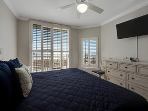 A bedroom with a large bed, a dresser, a ceiling fan, and a TV mounted on the wall.