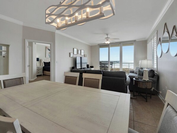 A spacious living area with a dining table, seating, a TV, and a balcony with a view.