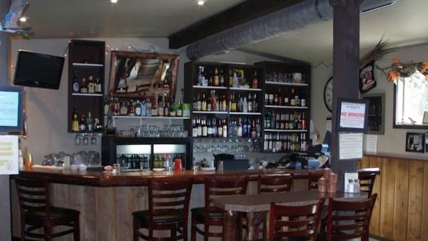 A bar area with wooden bar counters and stools, shelves with bottles, and a 'NO MINORS' sign.