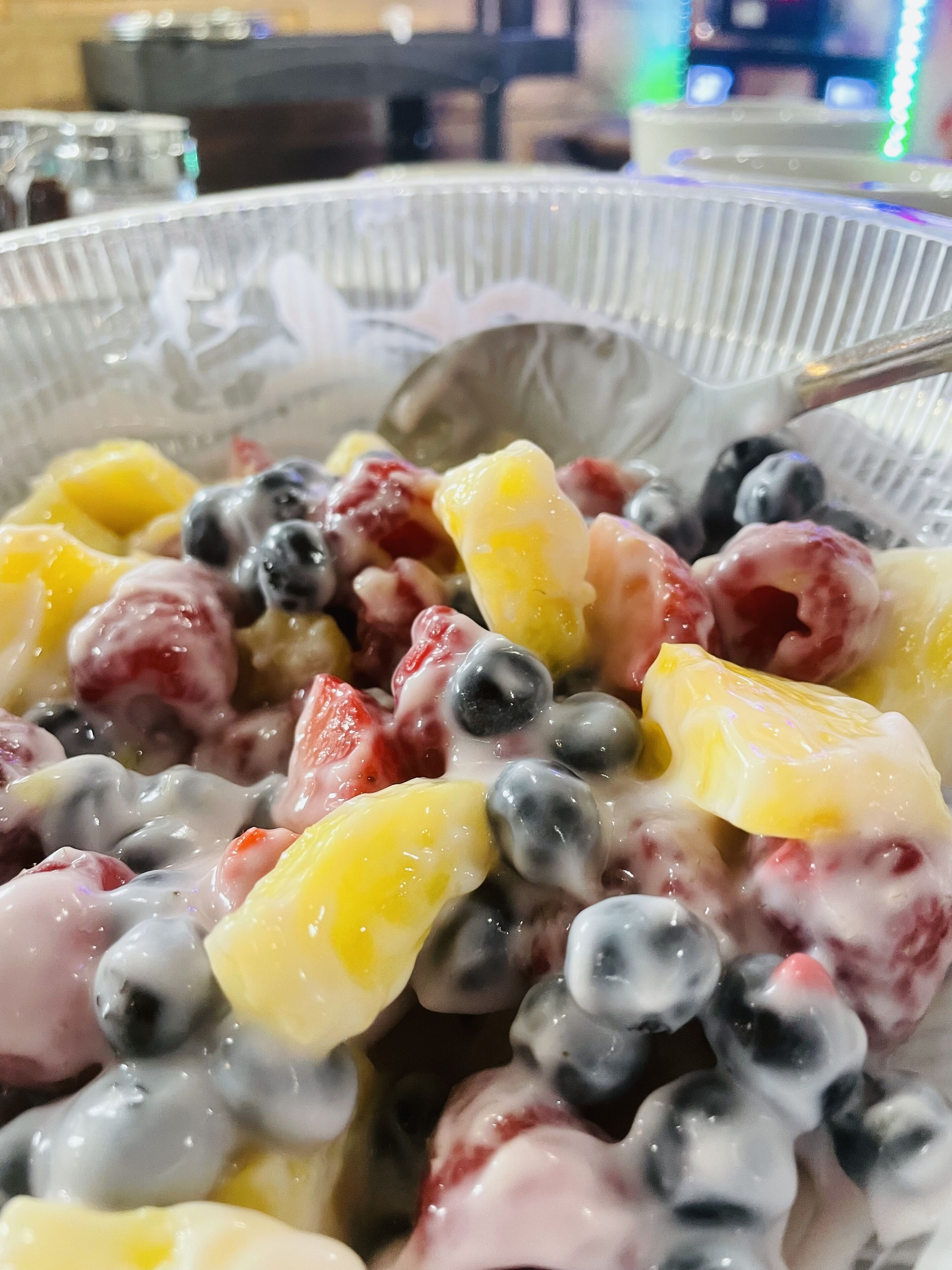 Un bol de salade de fruits contenant différents fruits, accompagné d’une cuillère.