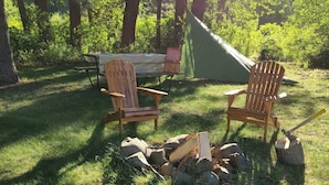 A campsite with two Adirondack chairs, a picnic table, a tent, and a fire pit with wood.