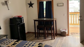 A bedroom with a bed, a desk with two chairs, a small refrigerator, a star decoration, and a window with curtains.