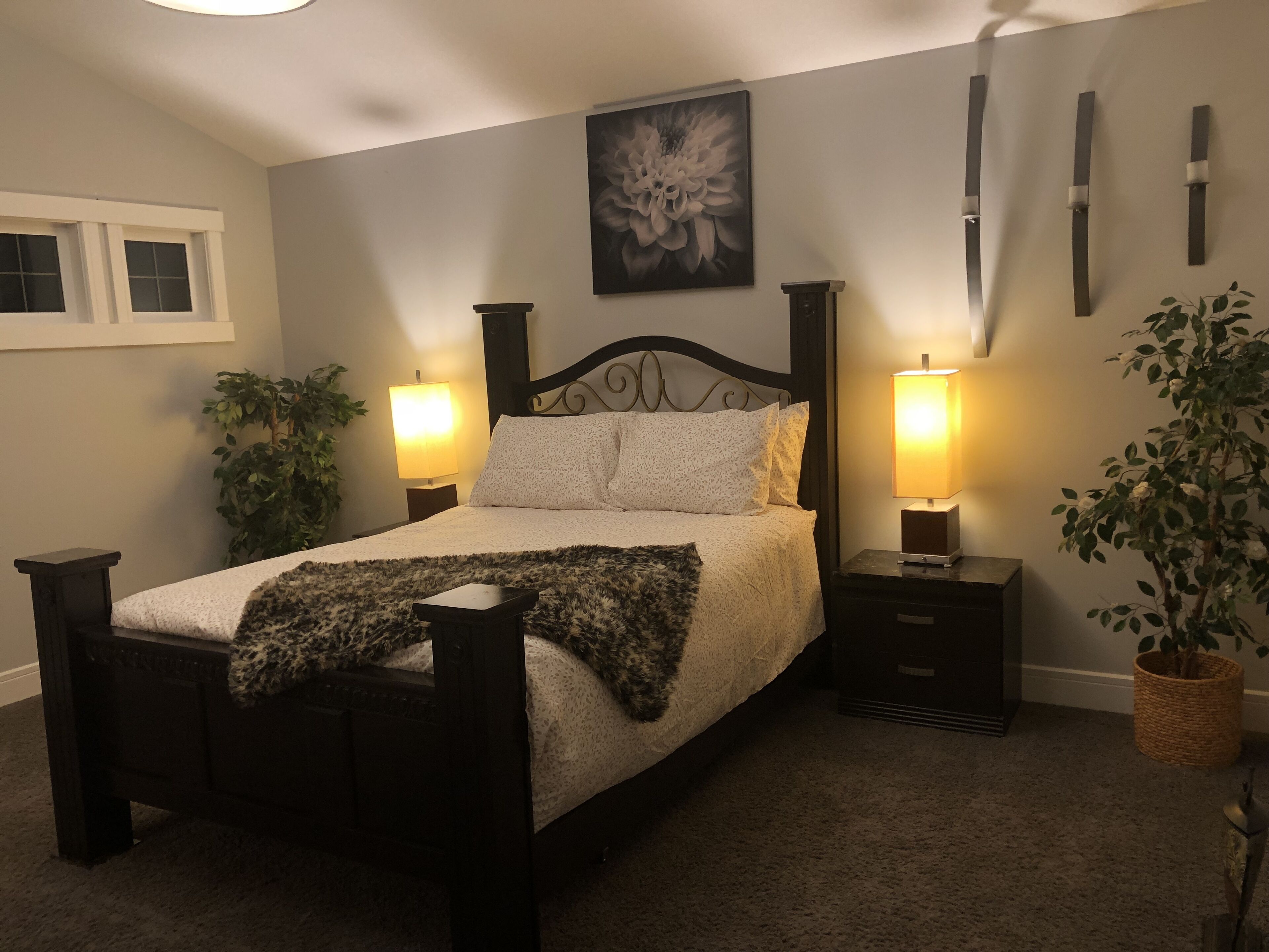 Ein Schlafzimmer mit einem Bett, zwei Nachttischen, einer Wandlampe, einem Blumentopf und einem Gemälde.
