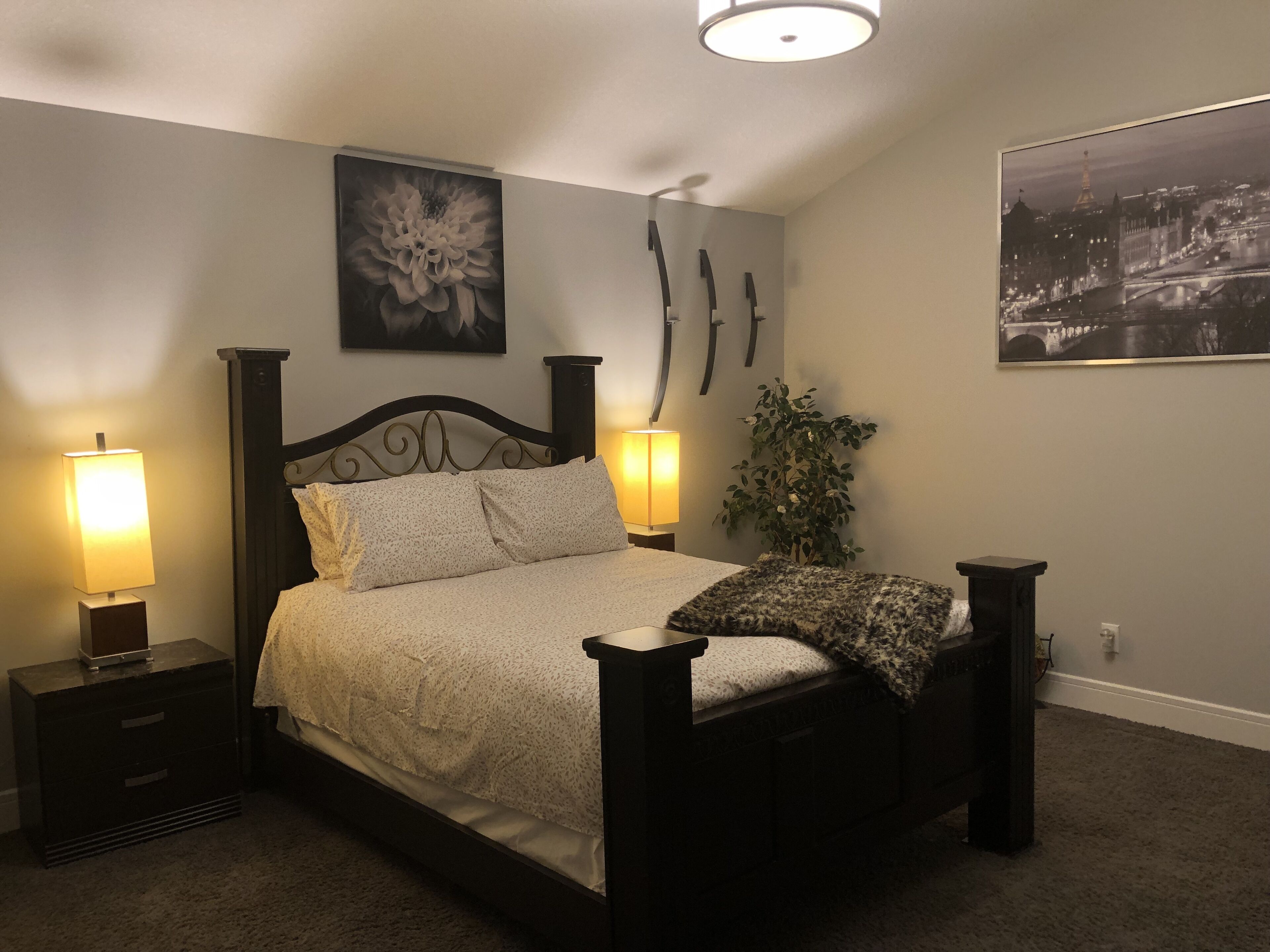 Ein Schlafzimmer mit einem Bett, zwei Nachttischen mit Lampen, einer Wandpflanze und zwei gerahmten Bildern.