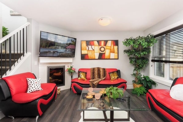 Una sala de estar moderna con un sofá rojo, una mesa de centro de vidrio y una chimenea.