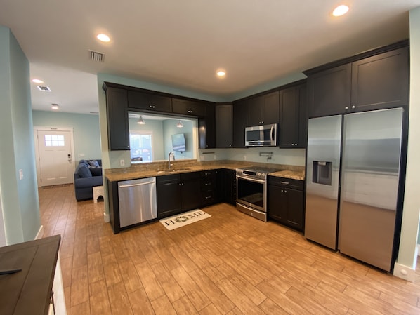 A modern kitchen with dark cabinets, stainless steel appliances, and a wooden floor.