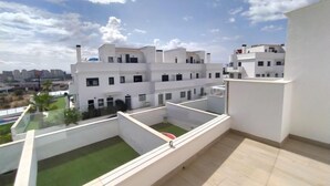 Un moderno complejo de apartamentos con varios edificios blancos, un jardín en la azotea y una vista despejada del paisaje urbano.