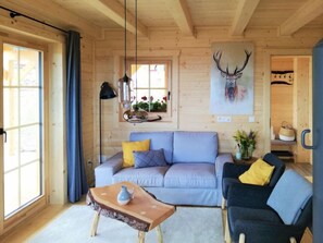 Un accogliente interno di una baita con un divano blu chiaro, una poltrona scura e un tavolino in legno.