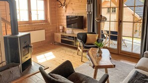 A cozy cabin interior with a fireplace, a TV, a dining area, and a large window offering a view of the outside. - Chalet Amsel by Interhome (Sirnitz - Hochrindl)