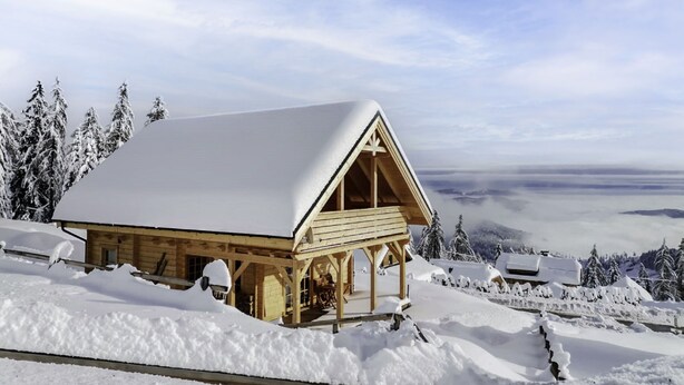 A wooden cabin with a snow-covered roof, surrounded by snow-covered trees and a mountainous landscape. - Chalet Amsel by Interhome (Sirnitz - Hochrindl)