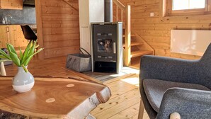 A cozy wooden cabin interior with a wood-burning stove, a dining table with a plant, and a gray chair. - Chalet Amsel by Interhome (Sirnitz - Hochrindl)