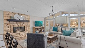 A spacious living room with a stone fireplace, a large TV, and a sofa with teal cushions. - Lake House - Six Bedroom House, Sleeps 14 (Sunrise Beach)