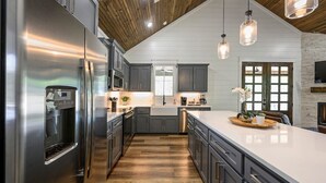 A modern kitchen with a large island, stainless steel appliances, and a wooden ceiling. - Platinum Ridge - Luxury One Bedroom with Bunk Nook (Broken Bow)