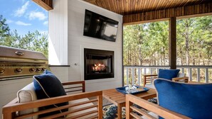 An outdoor deck with a grill and fireplace, wooden furniture, and a view of trees. - Platinum Ridge - Luxury One Bedroom with Bunk Nook (Broken Bow)