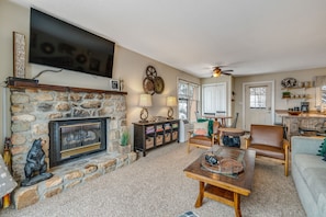 A cozy living room with a stone fireplace, a flat-screen TV mounted above it, and a comfortable seating area with a sofa and chairs. - Updated condo near Beech Mountain with deck, gas fireplace, mtn views - dogs OK (Beech Mountain)
