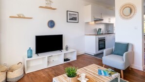 Ein modernes Wohnzimmer mit Flachbildfernseher, einer Couch, einem Couchtisch und einer Küche im Hintergrund.