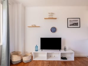 Ein modernes Wohnzimmer mit einem Flachbildfernseher auf einer weißen Unterhaltungsanlage, einer Uhr und zwei Regalen mit Dekoration.