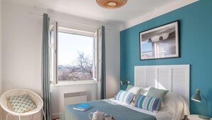 Ein Schlafzimmer mit einem Bett, einem Sessel, einem Fenster und einem Bild an der Wand.