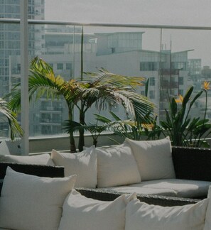 A balcony with a sofa and potted plants, overlooking a cityscape.
