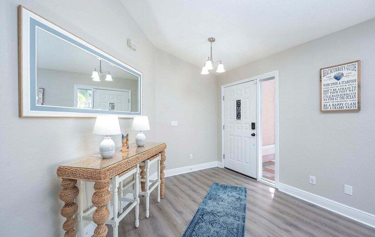 A hallway with a large mirror, a console table with two lamps, a blue rug, and a door with a sign.