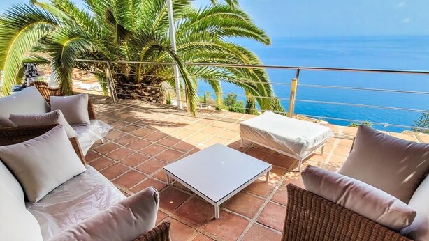 A patio with wicker furniture, a white table, and a view of the ocean. - Luxury villa with heated pool and sea views. (Salobreña)