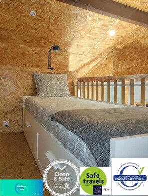 Quarto com teto de madeira, cama com colcha estampada, mesa de cabeceira e luminária na parede.