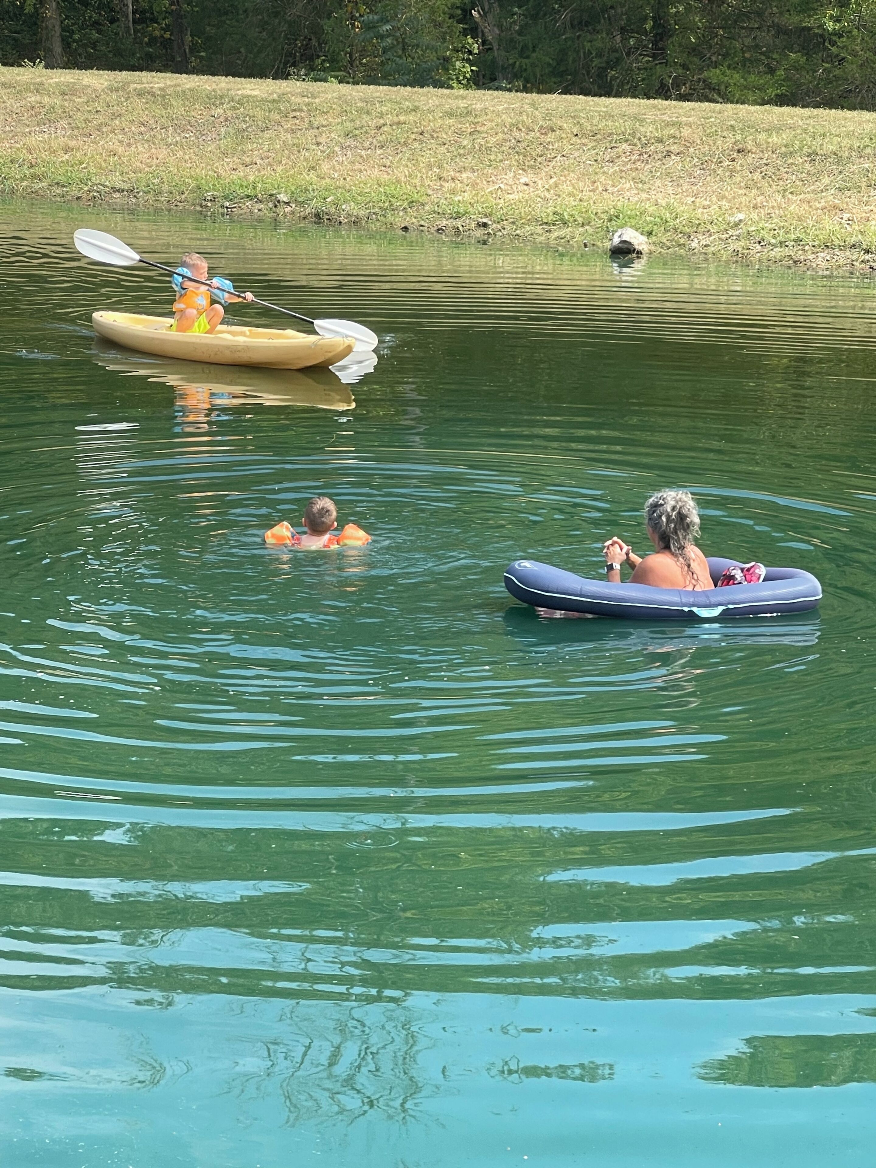 A calm lake with people in kayaks and a paddleboard.