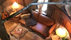 Interior acogedor de una cabaña con sofá de madera, una mesita de centro y una guitarra.