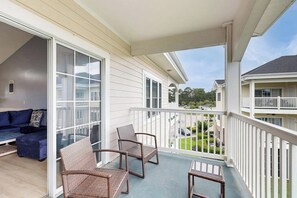 A balcony with wicker chairs and a small table, a blue sofa, and a view of neighboring houses. - Spacious condo with pool, fast WiFi, washer/dryer & central AC (Myrtle Beach)