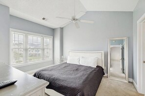 Une chambre à coucher avec un lit, un bureau, un ventilateur de plafond et une grande fenêtre.