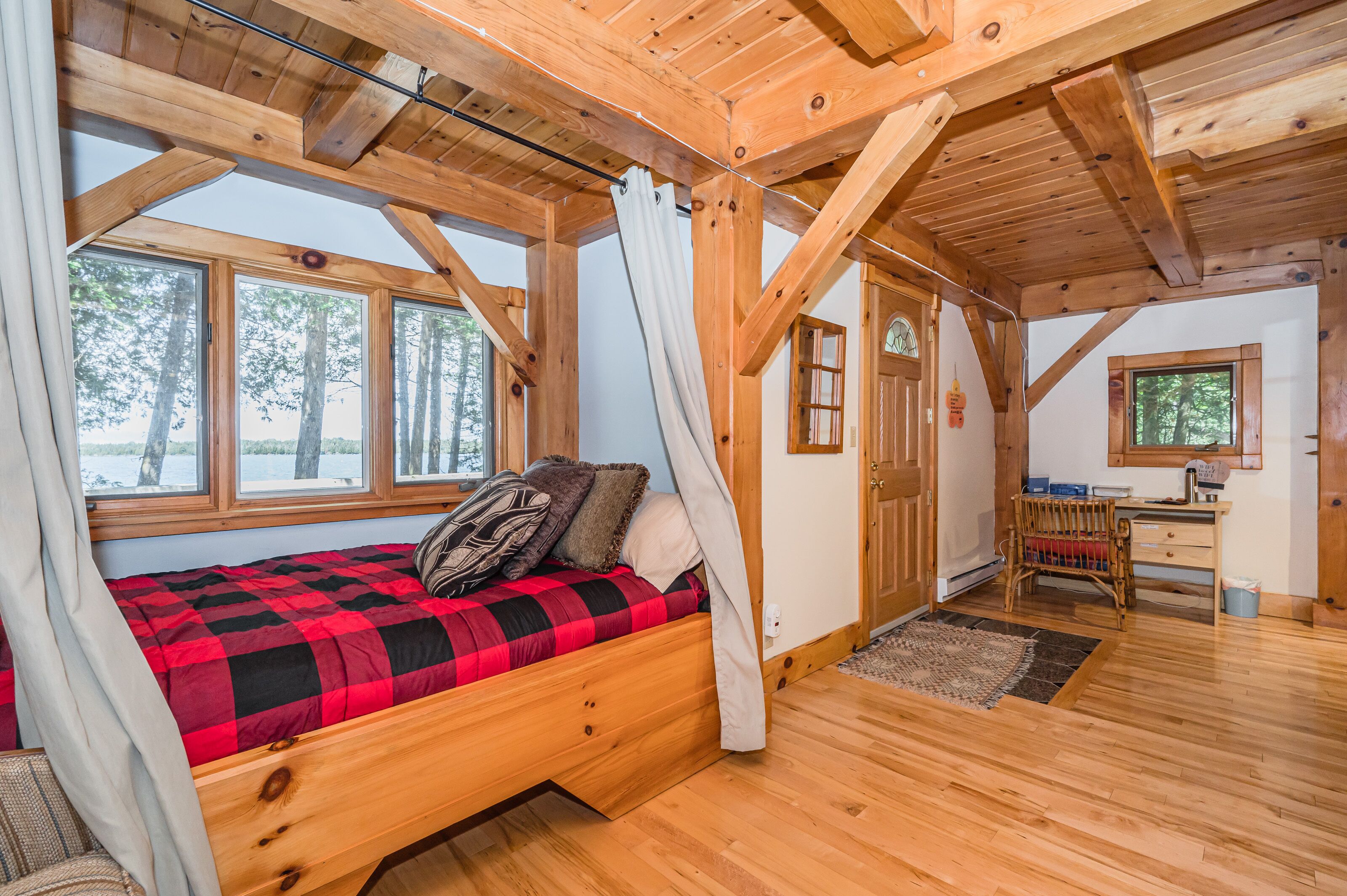 A cozy cabin with a wooden bed, large windows, a desk, and a view of trees.