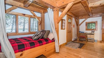 A cozy cabin with a wooden bed, large windows, a desk, and a view of trees.