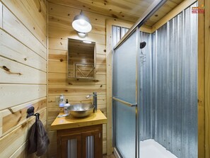 Une salle de bain rustique, avec des murs en bois, comprenant un lavabo, un miroir et une douche.