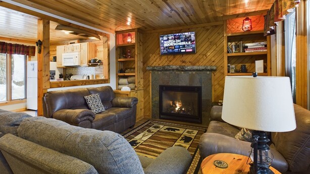 Una sala de estar acogedora con chimenea, sofás de cuero, un televisor montado en la pared y estanterías de madera con libros y adornos.