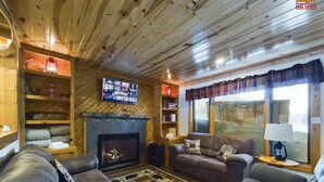 Interior acogedor de una cabaña con chimenea, sofás de cuero, estanterías de madera y un televisor.