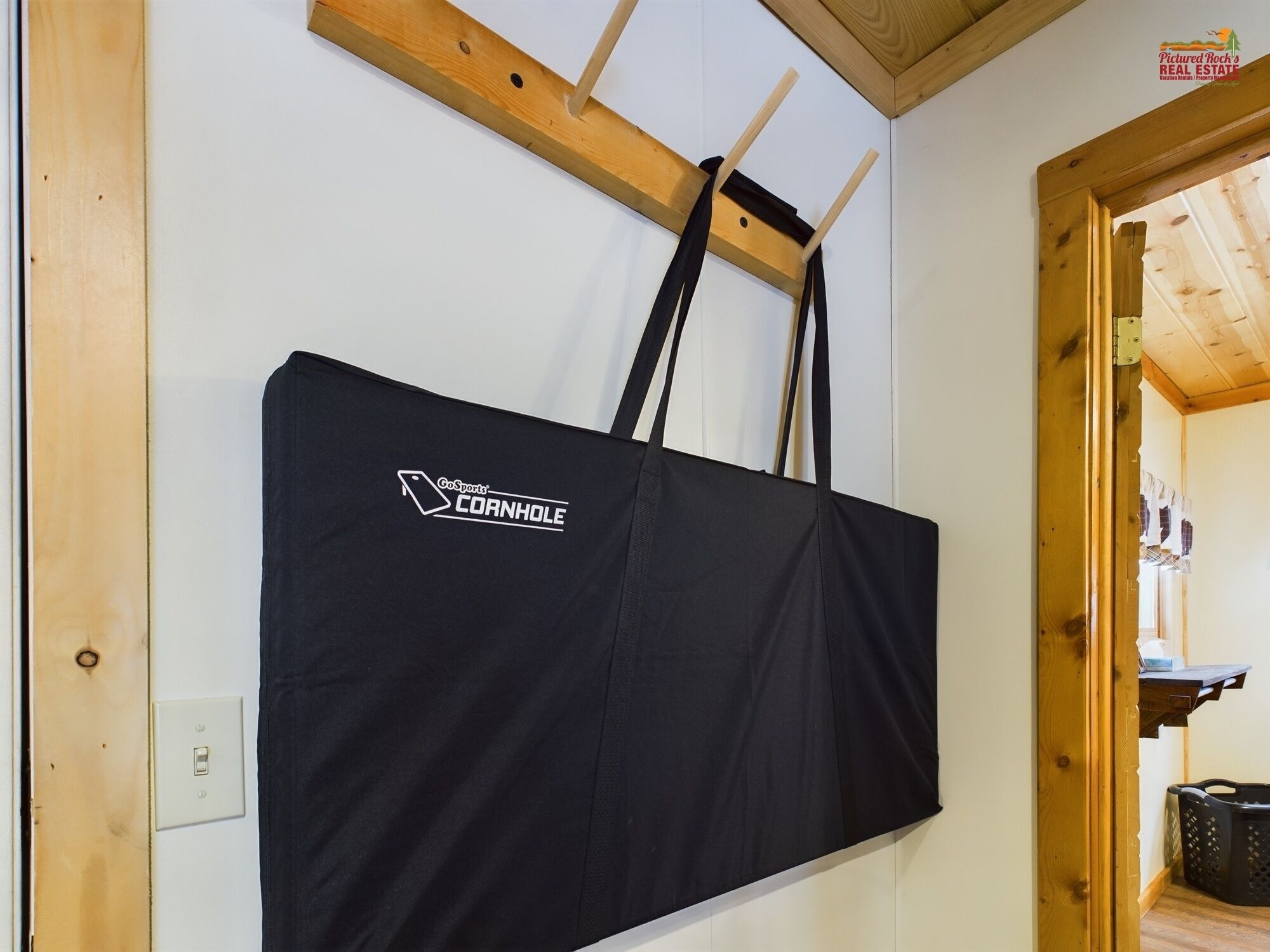 Un bolso negro colgado de una viga de madera en una habitación con paredes blancas y vigas de techo de madera.
