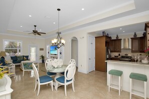 A spacious living area with a dining table, white chairs, and a ceiling fan.