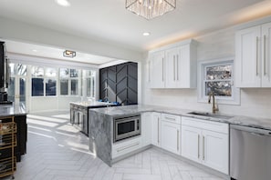 A modern kitchen with white cabinetry, a marble countertop, and a built-in microwave. - JAW-DROPPING SPRING LAKE "RESORT STYLE" HOME (Spring Lake)
