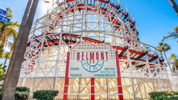 Ein Riesenrad im Belmont Park, mit Schildern, die Speisen, Geschäfte, einen Sportclub und Vergnügungsangebote ausweisen.