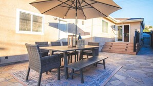 Un patio al aire libre con una mesa, sillas, una sombrilla grande y piso de piedra.