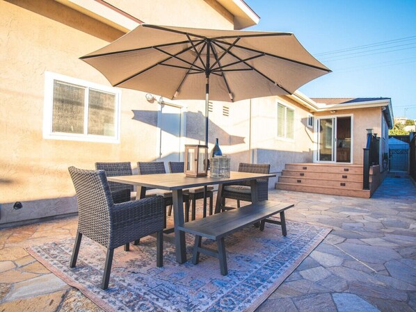 An outdoor patio with a table and chairs, a large umbrella, and a stone floor.